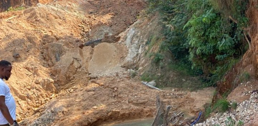 A man is positioned on a dirt road next to a river, representing the new Liberian mining company site