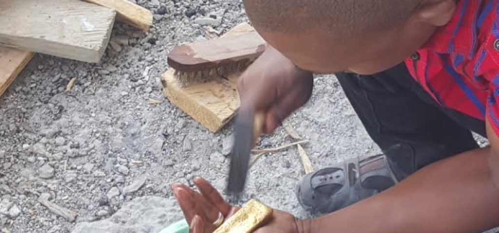 A man is kneeling to polishing materials and washing them into a bowl as part of gold processing for the New Liberia Mining Company