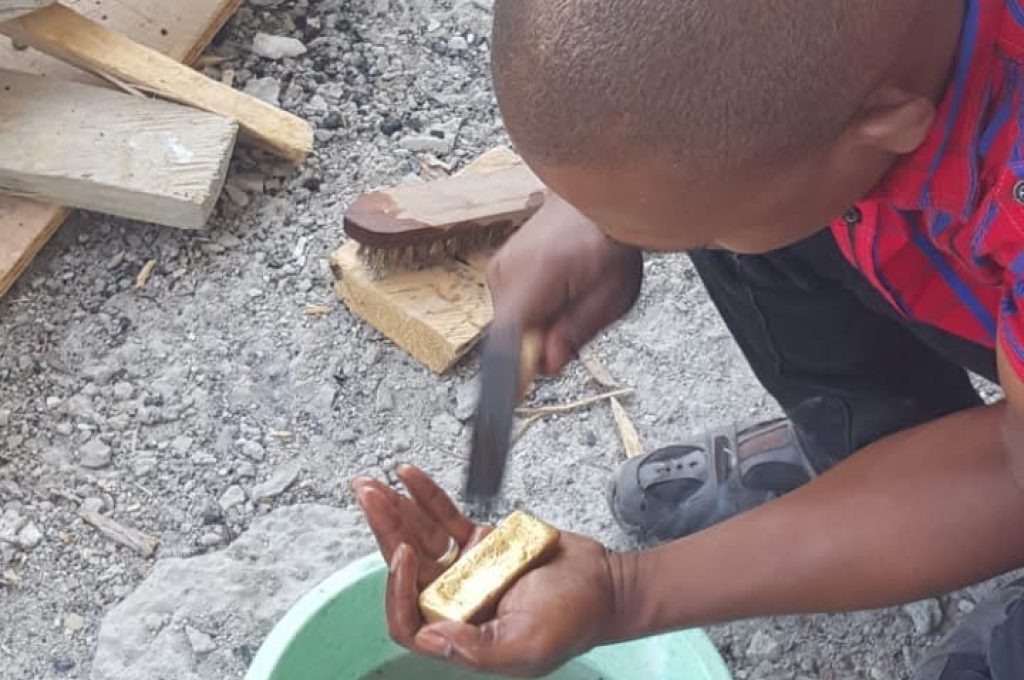 A man kneels, adding material to a bowl during the gold washing process at the New Liberian Mining Company site.
