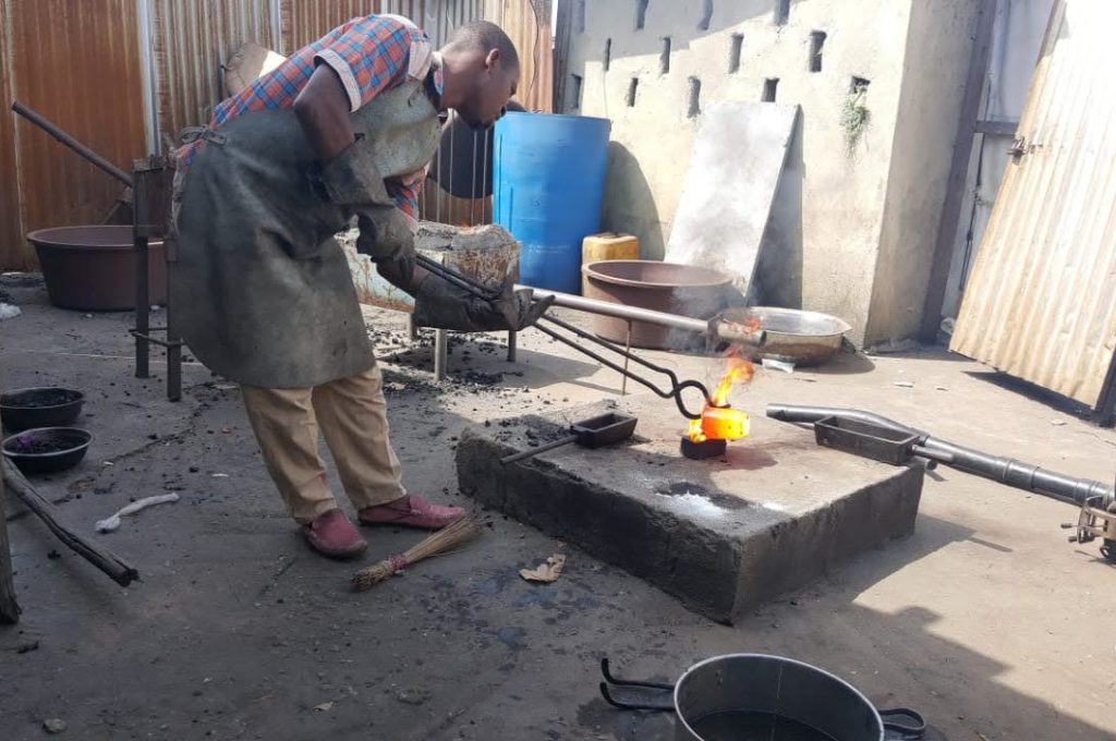 A man hammers a hot gold particle at the new Liberian mining company site, showcasing gold working techniques.