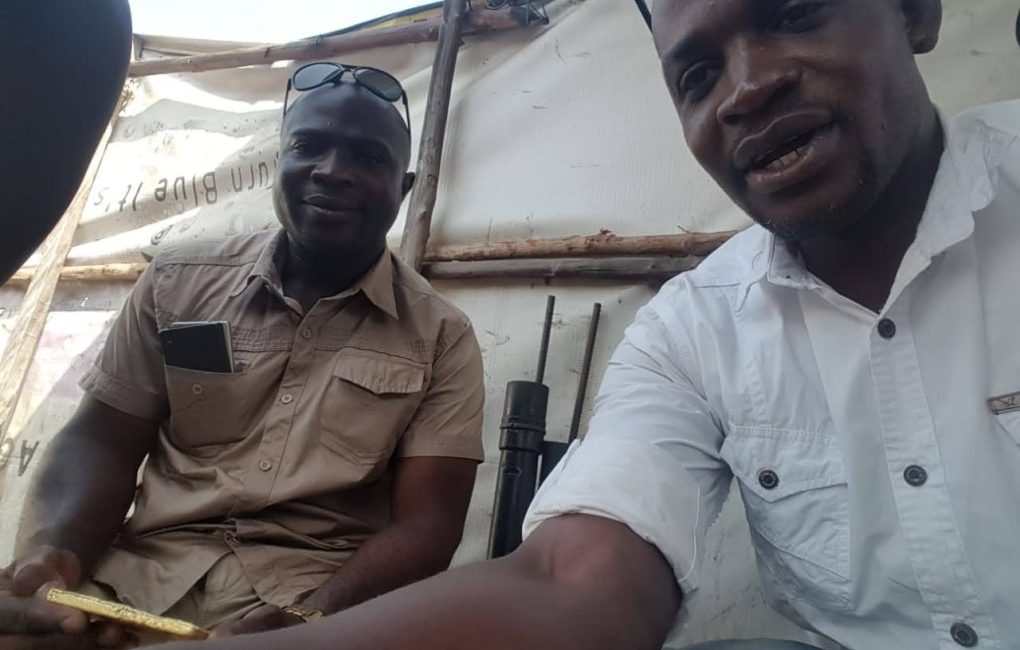 Two men seated in a tent, one with a gold in his hand, deliberating on gold processing and socio-economic impacts at the New Liberia's mining site