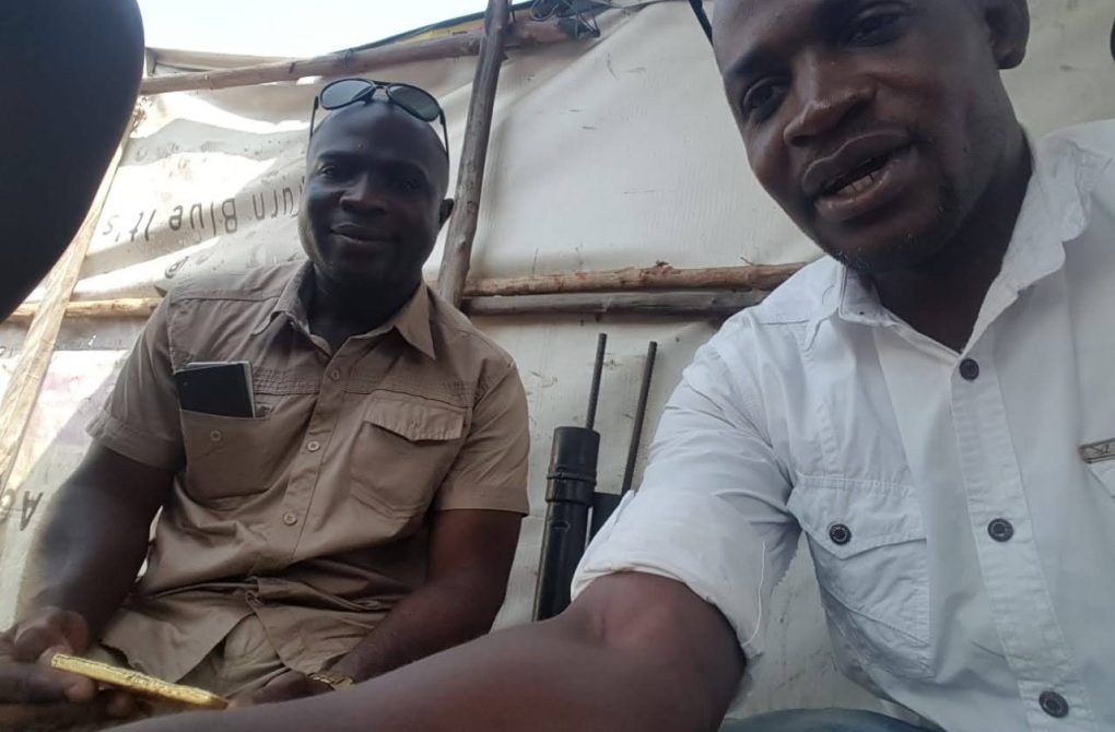 Two men seated in a tent, one with a gold in his hand, deliberating on gold processing and socio-economic impacts at the New Liberia's mining site