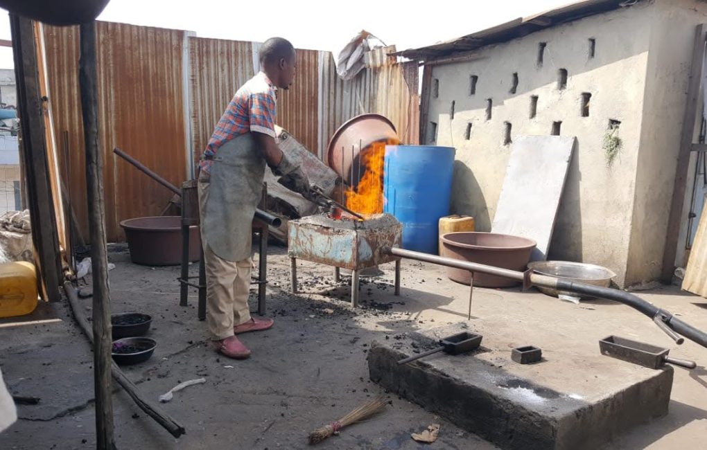 A man works on a metal object in a yard at the new Liberia mining company site, focused on gold mining activities.