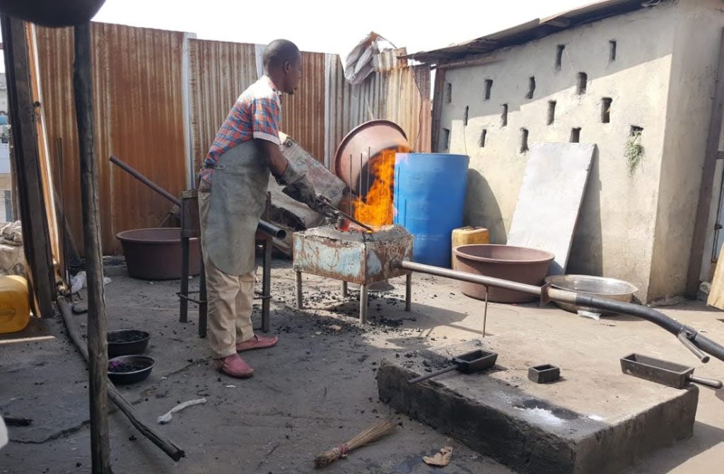 A man diligently works on a metal object in the yard of the New Liberian Mining Company, highlighting mining activities