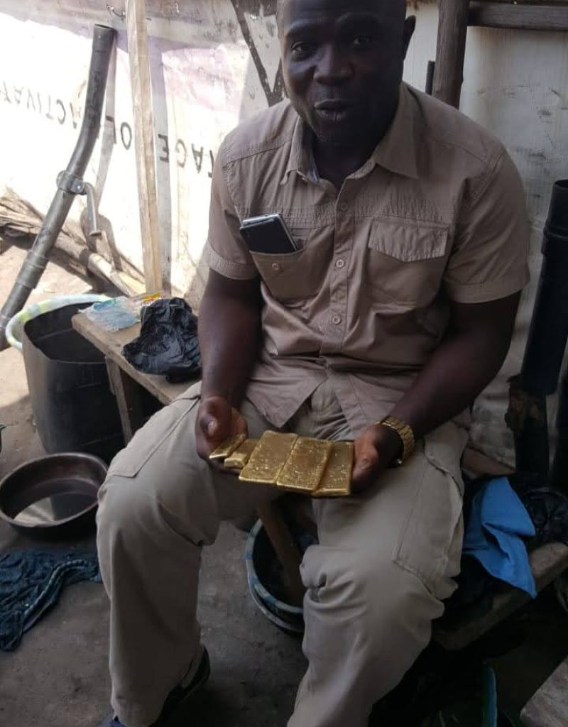 A man seated on a bench at the New Liberia Mining site, holding a gold bar in his hands