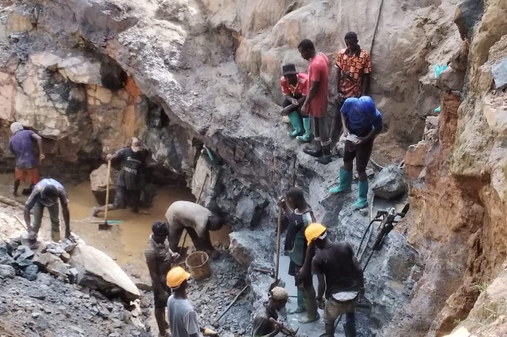 A group of workers in a mine, surrounded by a large pit, engaged in mining activities under a clear sky at the New Liberian Mining Company Site