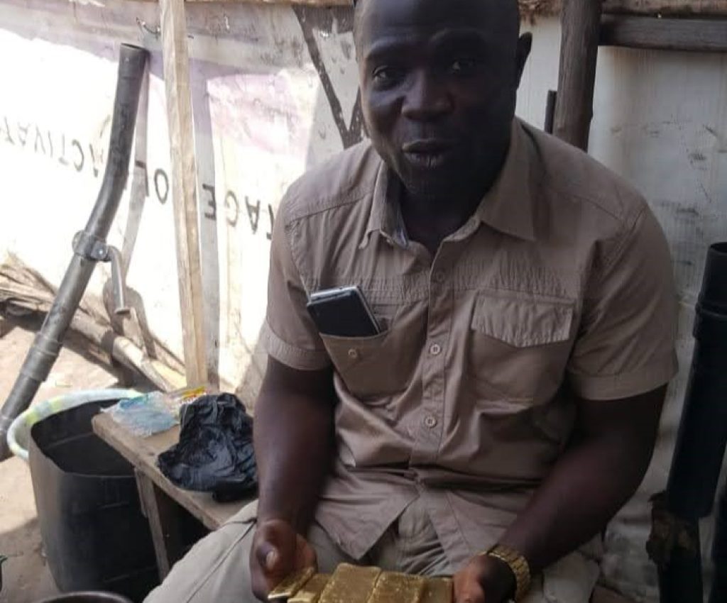 A man sits on a bench at New Liberian Mining Company, holding three large and two smaller processed gold bricks